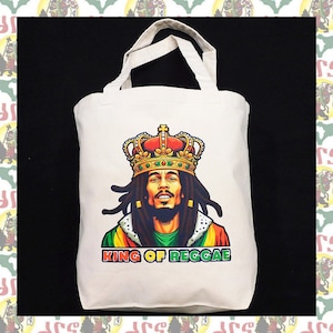 May include: A white canvas tote bag with a colorful illustration of Bob Marley wearing a crown and the text "KING OF REGGAE".
