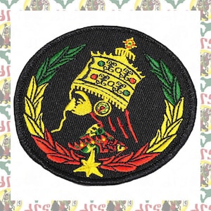 Puede incluir: Un parche bordado circular con fondo negro. El parche presenta el perfil de una persona que lleva una corona dorada y una túnica roja y verde. La persona está rodeada de una corona de hojas verdes y amarillas.