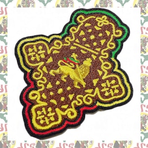 May include: Embroidered patch featuring a brown, gold, red, green, and black design. The patch has a central lion emblem and decorative scrollwork. The edges are outlined in black, red, and green.