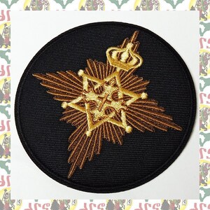 May include: A round, black embroidered patch with a gold starburst design. The starburst has a smaller, gold star in the center with a crown on top.