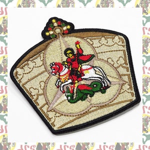 May include: Embroidered patch featuring a knight on horseback slaying a dragon. The knight is wearing red armor and holding a sword. The dragon is green and has red wings. The patch is surrounded by a gold crown with a black border.