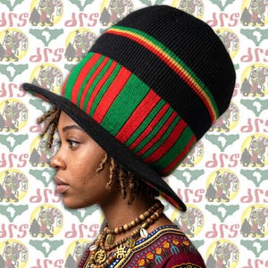 May include: A black, red, and green knit hat with a wide brim. The hat features vertical red and green stripes on the crown and a band of yellow, green, and red. The brim is black. The hat is worn by a person.