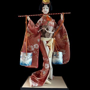 Japanese Geisha in Kimono Carrying Water Buckets Doll. This gorgeous and adorable geisha doll. Dressed in an opulent traditional costume.