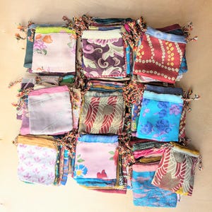 Puede incluir: Una colección de pequeñas bolsas de tela con cordón dispuestas en una cuadrícula. Cada bolsa presenta un patrón único, incluyendo estampados florales, formas geométricas y diseños abstractos en varios colores como rosa, azul y rojo.