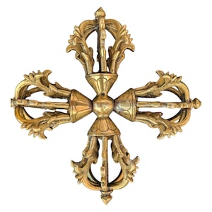 May include: A golden-colored, ornate vajra, a ritual object with a cross-like design. The vajra features intricate floral and geometric patterns, with a central sphere and four radiating arms. The object is likely made of brass or a similar metal.