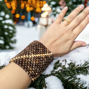 May include: A brown and beige beaded bracelet with a woven pattern. The bracelet is worn on a person's wrist.