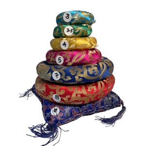 May include: A stack of seven round meditation cushions in various colors and patterns. The cushions are arranged in a pyramid shape, with the smallest cushion on top and the largest cushion on the bottom. The cushions are made of a soft, plush fabric and have a decorative embroidered design. The numbers 3, 3.5, 4, 5, 7, and 8 are written on the cushions.