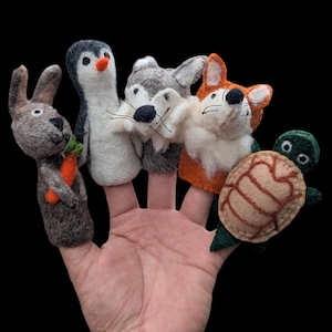May include: A set of five needle-felted animal finger puppets including a grey rabbit holding an orange carrot, a black and white penguin, a grey wolf, an orange and white fox, and a green turtle with a tan shell, all worn on fingers.