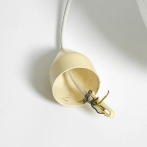 Puede incluir: Un componente de l&aacute;mpara en forma de l&aacute;grima, de color crema, con cables expuestos. La l&aacute;mpara est&aacute; suspendida por un cable blanco sobre un fondo blanco. Los cables son verdes, azules y rojos.