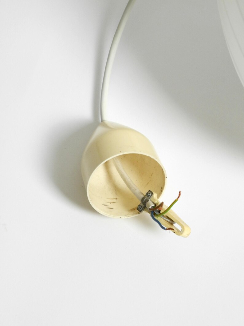 Puede incluir: Un componente de l&aacute;mpara en forma de l&aacute;grima, de color crema, con cables expuestos. La l&aacute;mpara est&aacute; suspendida por un cable blanco sobre un fondo blanco. Los cables son verdes, azules y rojos.