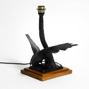 May include: Black metal table lamp with a bird design. The lamp has a wooden base and a black cord.