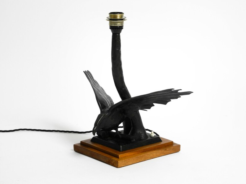 May include: Black metal table lamp with a bird design. The lamp has a wooden base and a black cord.
