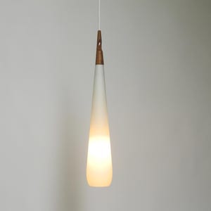 May include: A white frosted glass pendant light with a wooden top hangs from a white cord against a white wall.