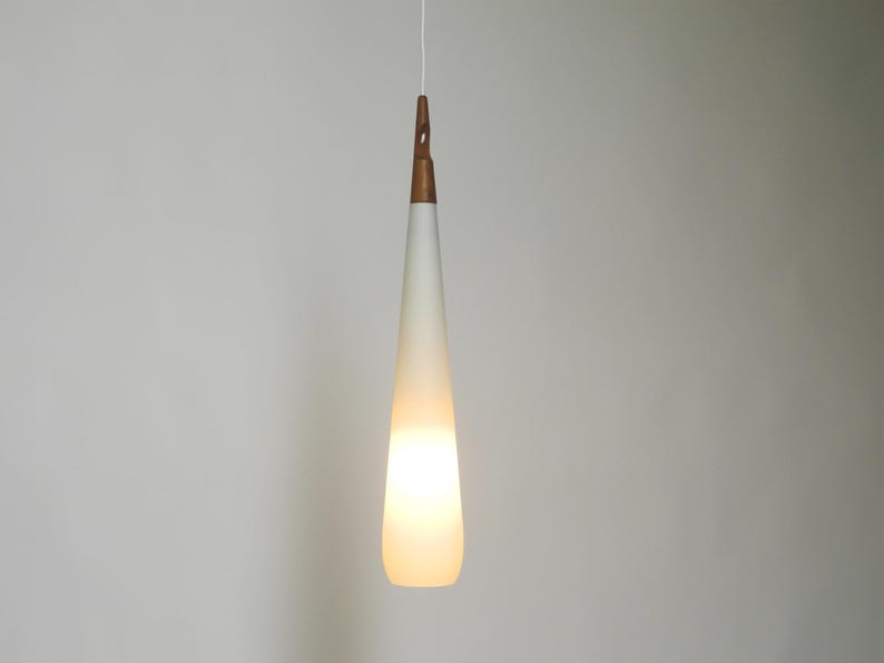 May include: A white frosted glass pendant light with a wooden top hangs from a white cord against a white wall.