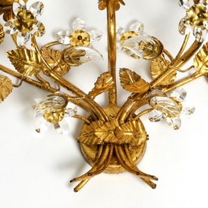 May include: Gold metal wall sconce with a floral design. The sconce features leaves and flowers made of metal and crystal accents.