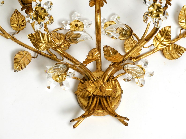 May include: Gold metal wall sconce with a floral design. The sconce features leaves and flowers made of metal and crystal accents.