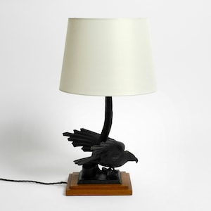 May include: A black table lamp with a white lampshade. The base of the lamp is a carved wooden bird with outstretched wings.
