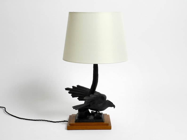 May include: A black table lamp with a white lampshade. The base of the lamp is a carved wooden bird with outstretched wings.