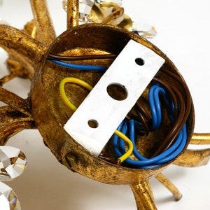 May include: Close-up of the back of a gold-toned chandelier with crystal accents. The wiring is visible inside the base.