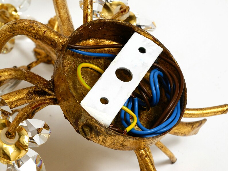 May include: Close-up of the back of a gold-toned chandelier with crystal accents. The wiring is visible inside the base.