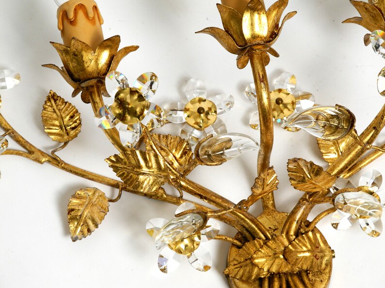 May include: Gold metal wall sconce with a floral design. The sconce features leaves, flowers, and crystal accents.