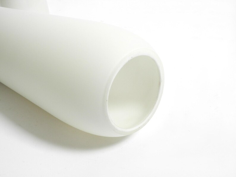 May include: White ceramic vase with a smooth, rounded shape and a wide opening. The vase is designed with a unique twist in the middle, creating a modern and elegant look.