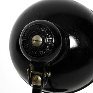 Puede incluir: L&aacute;mpara de escritorio de metal negro con una pantalla redonda y un brazo ajustable de plata. La l&aacute;mpara tiene una base de metal negro y una pantalla de metal negro con un tornillo de plata en la parte superior. La pantalla tiene el texto "DESIGN  PATENT  MK  MADE IN  ENGLAND".