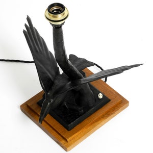 May include: A black metal table lamp shaped like a pair of birds with a gold-colored socket. The lamp is on a wooden base.