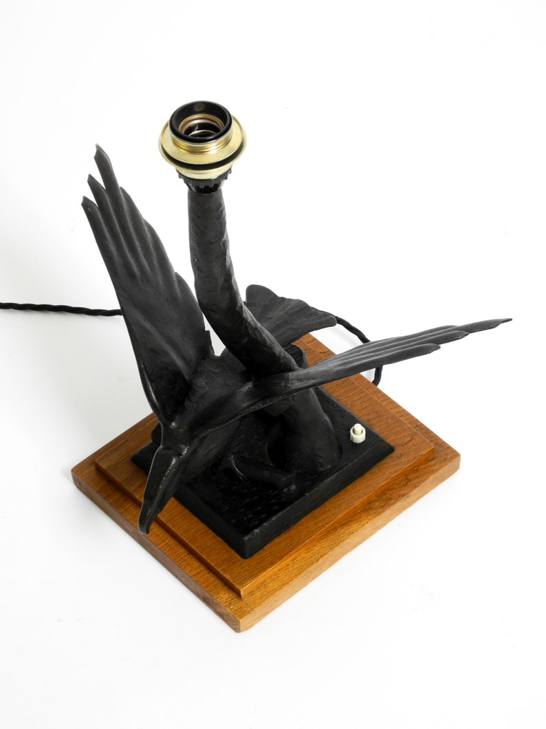 May include: A black metal table lamp shaped like a pair of birds with a gold-colored socket. The lamp is on a wooden base.