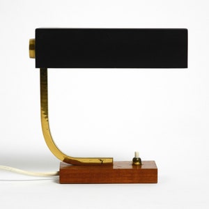 May include: A black and gold desk lamp with a wooden base. The lamp has a rectangular shade and a curved arm.