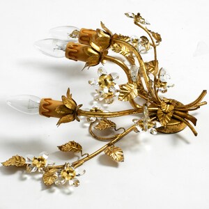 May include: Gold metal wall sconce with a floral design. The sconce has three light bulbs and is decorated with crystal accents.