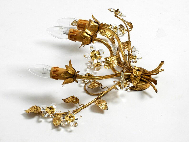 May include: Gold metal wall sconce with a floral design. The sconce has three light bulbs and is decorated with crystal accents.
