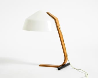 May include: A contemporary desk lamp featuring a white, cone-shaped shade and a curved wooden frame. The lamp has a rectangular wooden base and a black cylindrical support. A white power cable extends from the base.