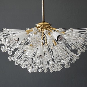 Peut inclure: Un lustre vintage de style milieu du siècle avec une finition en laiton et des détails en cristal transparent. Le luminaire comporte plusieurs ampoules et un design en forme d'éclat d'étoile, créant un look glamour. Suspendu au plafond.
