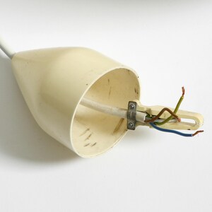 Puede incluir: Un accesorio el&eacute;ctrico de color crema con cables expuestos. El accesorio tiene forma c&oacute;nica con un cable blanco que se extiende desde la parte superior. Los cables son verdes, marrones y azules y est&aacute;n sujetos por una abrazadera met&aacute;lica.