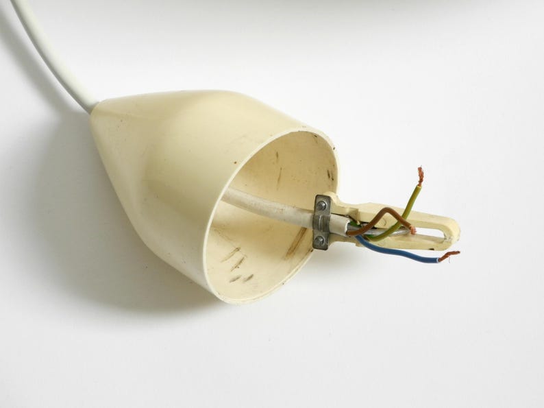 Puede incluir: Un accesorio el&eacute;ctrico de color crema con cables expuestos. El accesorio tiene forma c&oacute;nica con un cable blanco que se extiende desde la parte superior. Los cables son verdes, marrones y azules y est&aacute;n sujetos por una abrazadera met&aacute;lica.