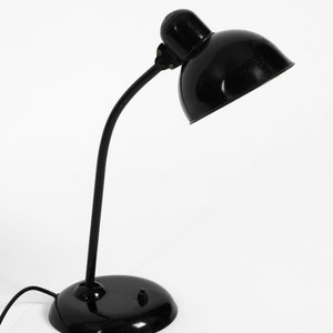 Puede incluir: Una l&aacute;mpara de escritorio negra con un brazo curvo y una pantalla redonda. La l&aacute;mpara tiene un dise&ntilde;o sencillo y est&aacute; hecha de metal.