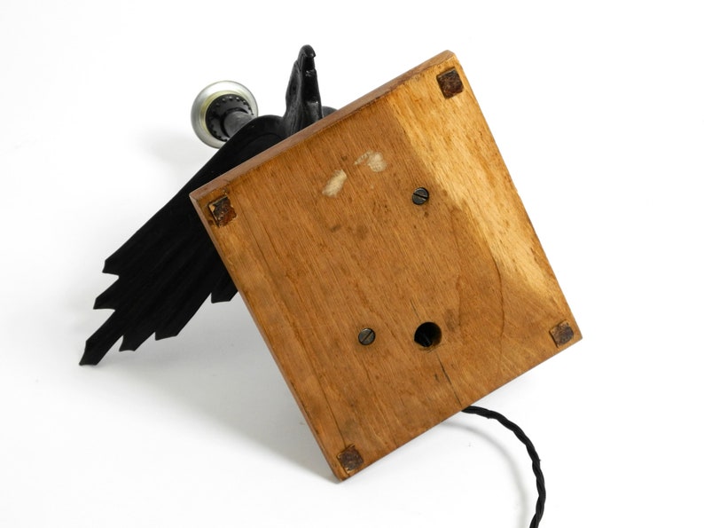 May include: A black metal lamp with a bird design and a wooden base. The lamp has a cord and a light bulb.