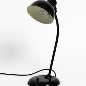 Puede incluir: Una l&aacute;mpara de escritorio negra con un brazo flexible y una pantalla interior blanca. La l&aacute;mpara tiene una base redonda y un cable.