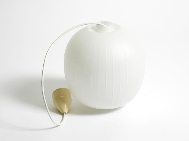 Puede incluir: L&aacute;mpara colgante esf&eacute;rica blanca con ranuras verticales. La l&aacute;mpara tiene un cable blanco y un elemento en forma de cono dorado. El dise&ntilde;o es minimalista y moderno, adecuado para la iluminaci&oacute;n interior.