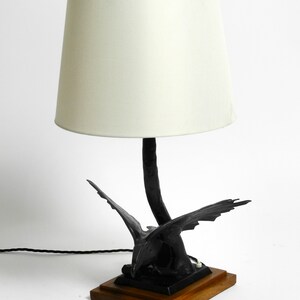 May include: A black table lamp with a white lampshade. The base of the lamp is a stylized sculpture of a bird in flight.