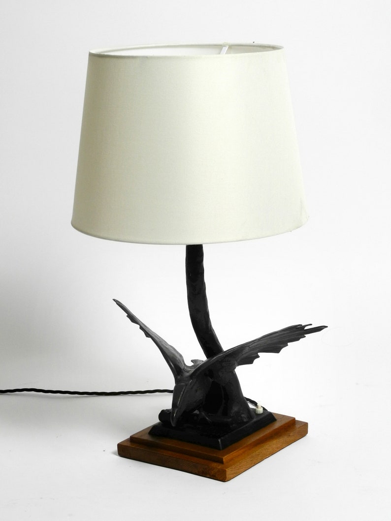 May include: A black table lamp with a white lampshade. The base of the lamp is a stylized sculpture of a bird in flight.