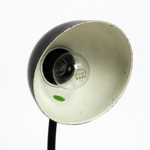 Puede incluir: L&aacute;mpara de escritorio negra y blanca con interior blanco y brazo de metal negro. La l&aacute;mpara tiene una bombilla de vidrio transparente con el texto "KESS 40 W" impreso en ella.