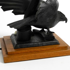 May include: A black carved eagle lamp with a wooden base. The eagle is perched on a branch with its wings spread. The lamp has a black cord and a white switch.