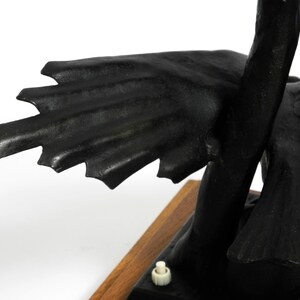 May include: Black metal sculpture of a bird with outstretched wings. The bird is perched on a wooden base with a small white switch.
