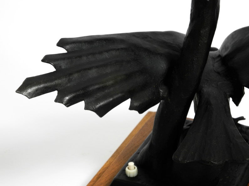 May include: Black metal sculpture of a bird with outstretched wings. The bird is perched on a wooden base with a small white switch.