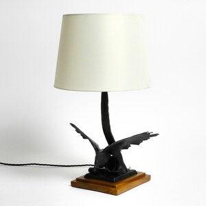May include: A black table lamp with a white lampshade. The base of the lamp is a stylized sculpture of a bird with outstretched wings.
