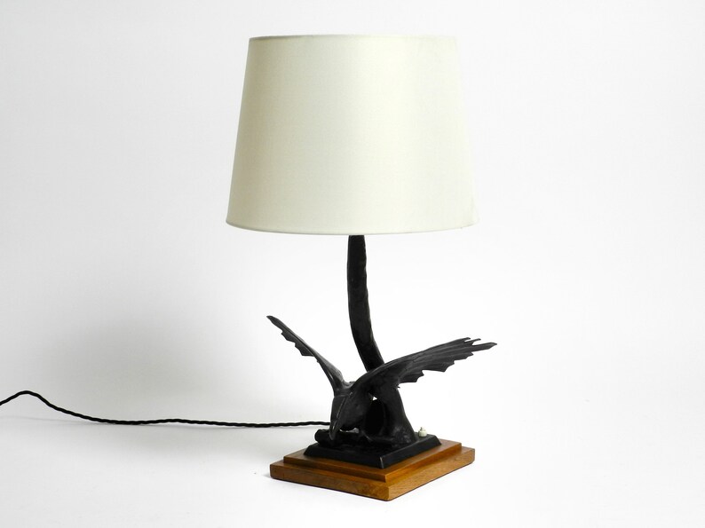 May include: A black table lamp with a white lampshade. The base of the lamp is a stylized sculpture of a bird with outstretched wings.