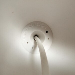 May include: White ceiling fixture with a white cord and a white plastic cover with the text "LUXUS MADE IN SWEDEN".