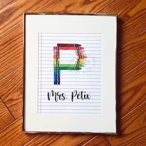 May include: A framed print with a colorful letter "P" made of crayons on a sheet of lined paper. The text "Mrs. Petix" is written below the letter.